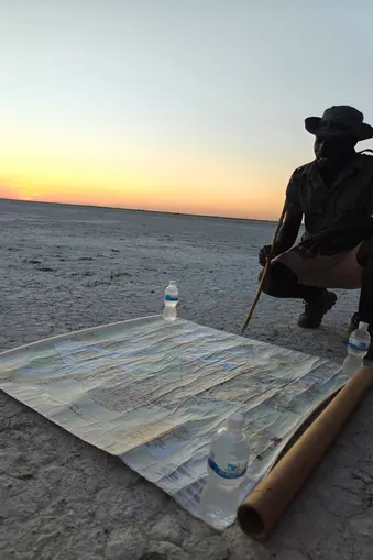 Gids toont een landkaart op de witte zoutvlakte van Makgadikgadi bij zonsondergang