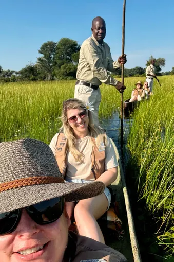Toeristen in een traditionele mokoro-kano varen door het hoge gras van de Okavango Delta, begeleid door lokale gidsen
