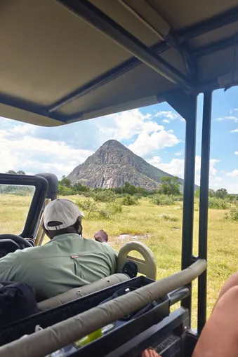 Uitzicht vanuit een safari-jeep op de Tsodilo Hills in Botswana met een indrukwekkende rotsformatie in de verte.