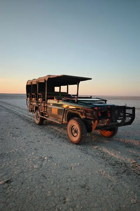 Open safari-jeep op de uitgestrekte, droge vlakte van de Makgadikgadi-zoutpannen bij zonsondergang.