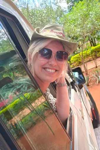 Vrolijke vrouw met zonnebril en safaripet kijkt uit het raam van een safari-jeep tijdens een rondreis door Kenia