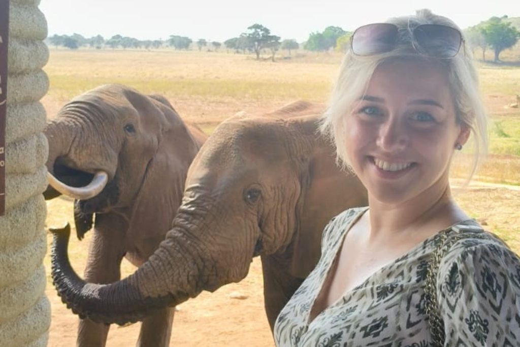Glimlachende vrouw poseert bij twee jonge olifanten in het Taita Hills Wildlife Sanctuary in Kenia