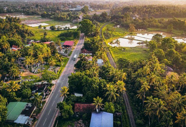 Luchtfoto van een landelijk dorp met rijstvelden, palmbomen en een spoorlijn in Sri Lanka bij zonsondergang