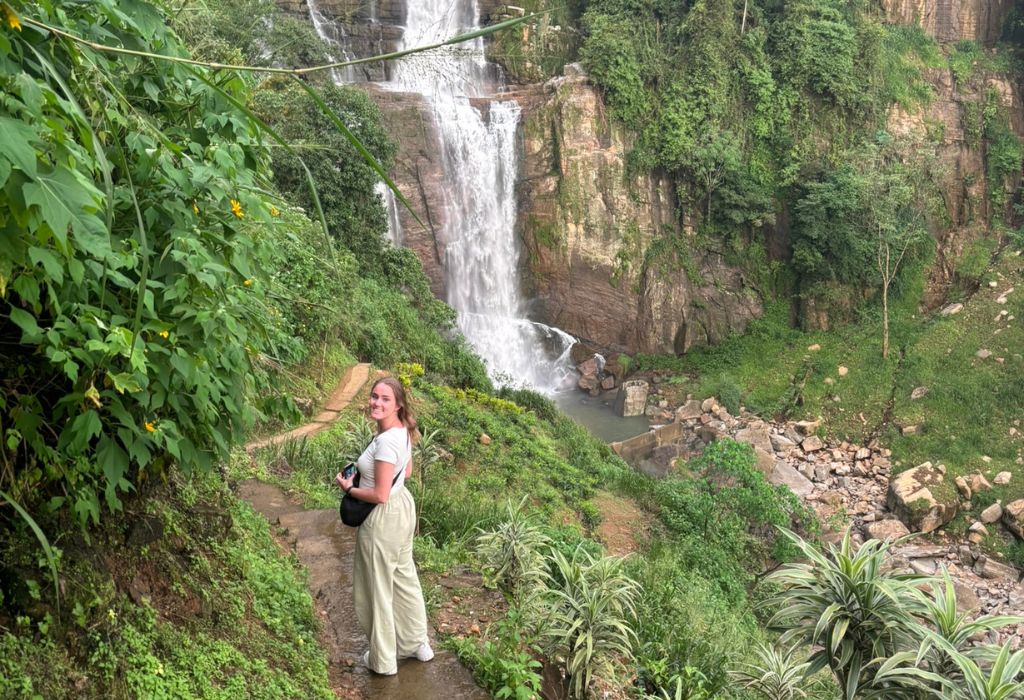 Reiziger staat op een pad bij een waterval in de weelderige natuur van centraal Sri Lanka, omringd door tropische begroeiing.
