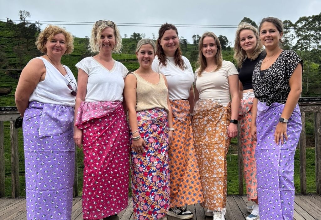 Reisgroep van Best of Travel in kleurrijke traditionele kleding, poserend voor een theeplantage in de heuvels van Sri Lanka."