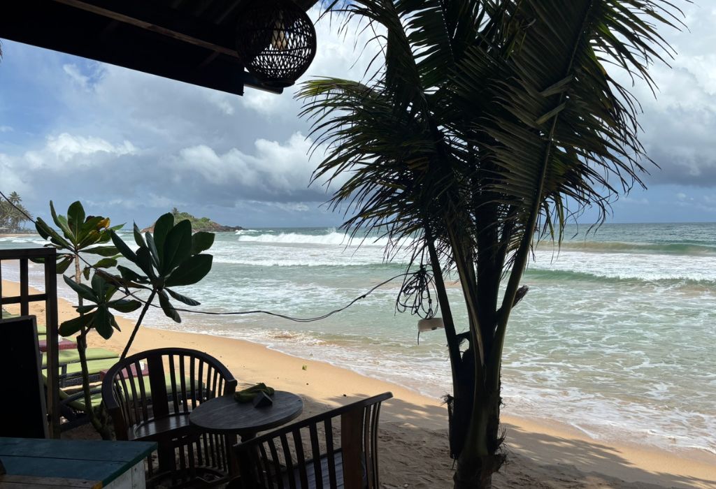 Uitzicht vanaf een strandcafé op de golven van Hikkaduwa, omringd door palmbomen en een ontspannen sfeer aan de zuidkust van Sri Lanka.